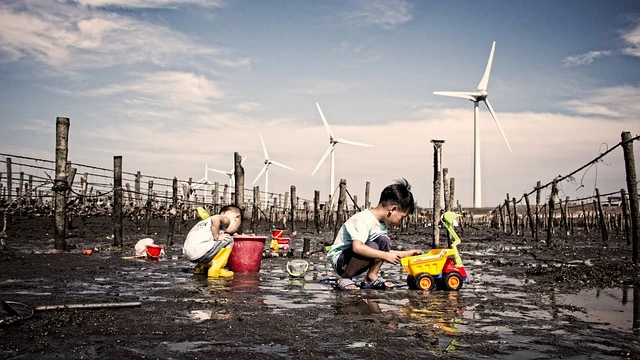 Children playing in polluted industrial area with wind turbines in the background, highlighting the environmental and health impact of industrial pollution.